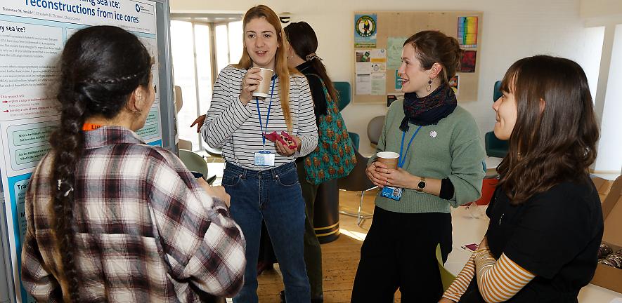 Four women discuss a poster with coffee