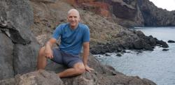 Jonathan Nitschke sitting on rocks by the sea, smiling at camera