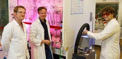 Three men in lab coats in the lab smiling at camera