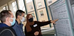 Three students in protective Covid masks looking at research poster
