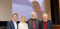 Ben Feringa, Sally Boss, John Hopkins & Jeremy Sanders looking ahead, standing in front of photo of Alex Hopkins on screen