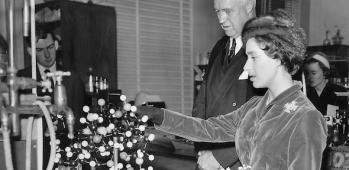 Princess Margaret & Lord Todd looking at a model of vitamin B-12 in a black and white photo from 1958.