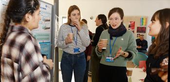 Four women discuss a poster with coffee