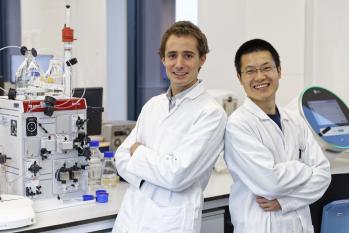 Two scientists in lab coats stand in a laboratory.