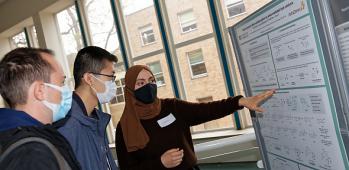 Three students in protective Covid masks looking at research poster
