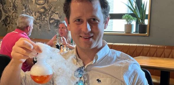 Ben Pilgrim smiling at camera holding a foaming test tube