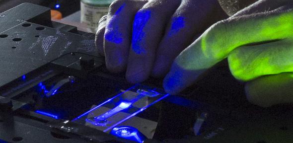 Gloved hands probing a microfluidic device in laser light