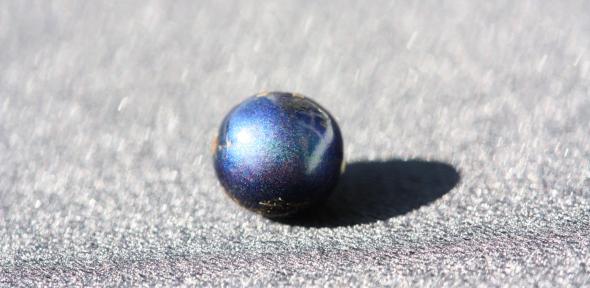 A single iridescent blue pollia condensata berry on a grey background