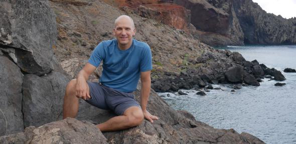 Jonathan Nitschke sitting on rocks by the sea, smiling at camera