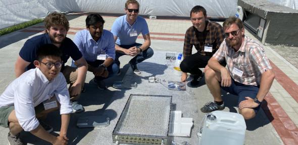 The team members sitting by the instrument looking at camera