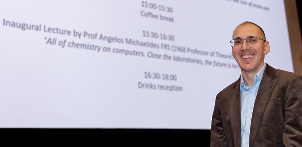 Angelos smiling at camera in front of a screen with the name of his talk