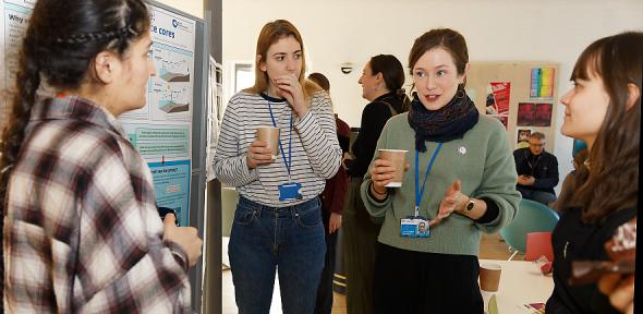 Four women discuss a poster with coffee