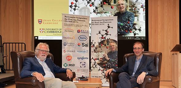 Ian Paterson, left, and Jonathan Goodman, right, sit on chairs in front of the symposium banners.