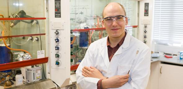 Jonathan Nitschke in lab coat & protective glasses smiling at camera