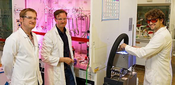 Three men in lab coats in the lab smiling at camera