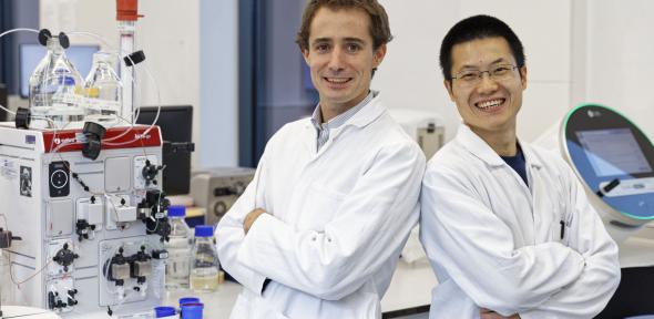 Two scientists in lab coats stand in a laboratory.