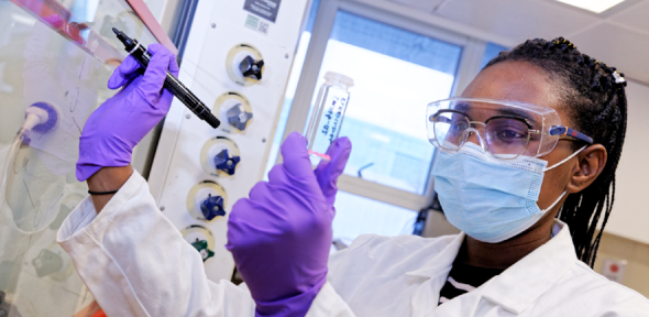 Scientist in facemask holds a test tube.