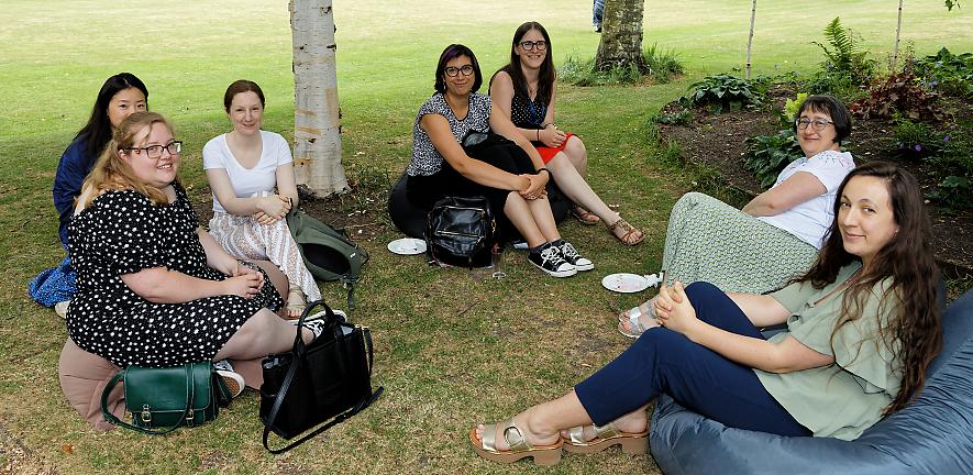 Group of staff sitting on bean bags on lawn smiling at camera