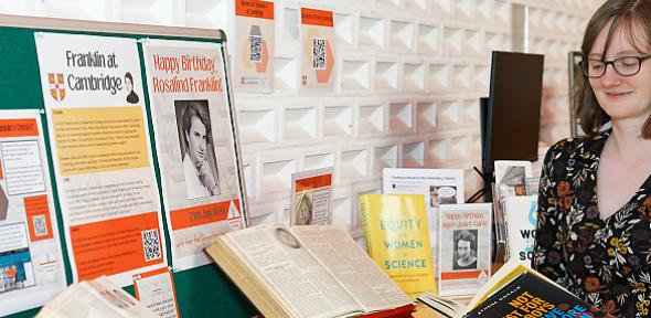 Megan Holman reading a book next to a table in the library with all the exhibition items displayed