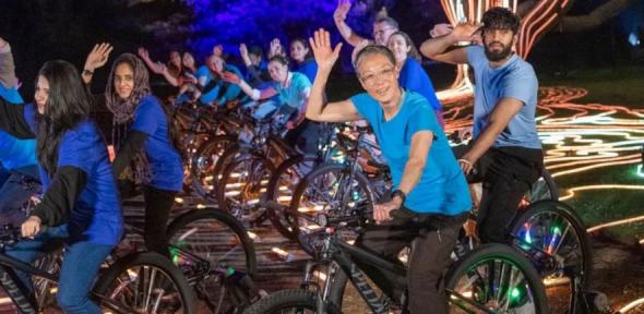 Katherine and other cyclists waving at camera with lit tree in background