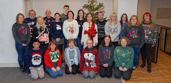 Staff members wearing silly Christmas jumpers in front of Christmas tree in lobby