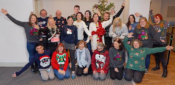 Staff members wearing silly Christmas jumpers in front of Christmas tree in lobby