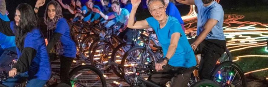 Katherine and other cyclists waving at camera with lit tree in background