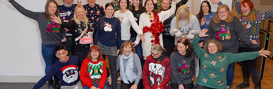 Staff members wearing silly Christmas jumpers in front of Christmas tree in lobby