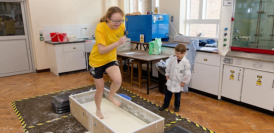 Open day volunteer running on cornflour slime in a vat, watched by a child