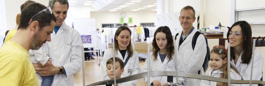 A group of adults and children in lab coats smiling at an experiment