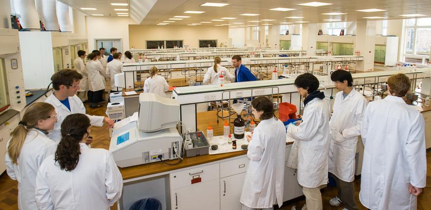 long view of chemistry students in lab coats working in chem teach labs
